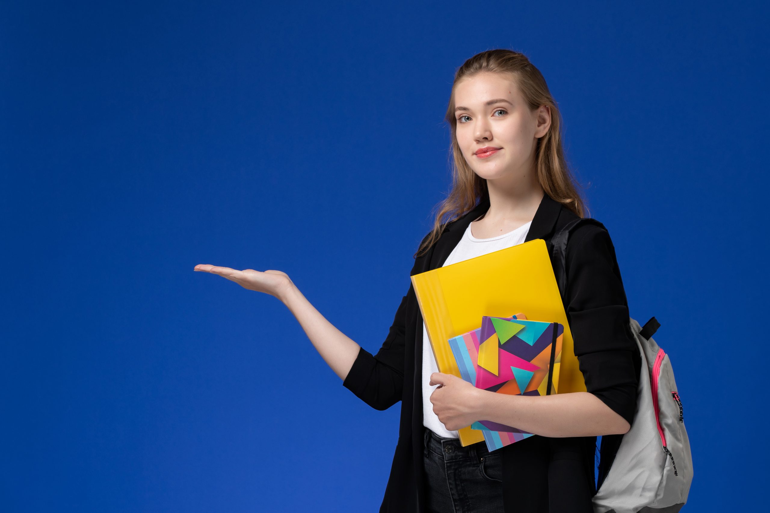 front-view-female-student-white-shirt-black-jacket-wearing-backpack-holding-files-with-copybooks-blue-wall-college-university-lessons