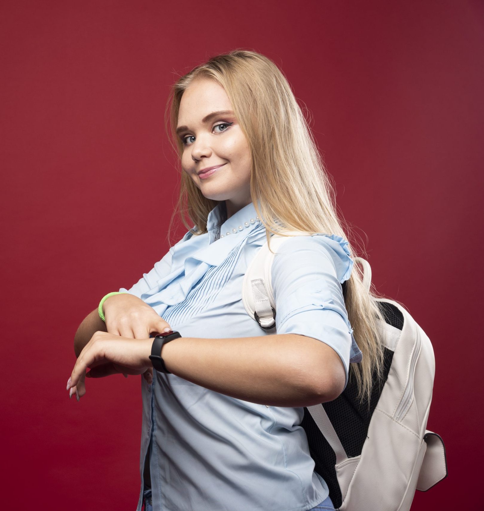Young blonde schoolgirl goes back to school and checks the time at her watch. High quality photo