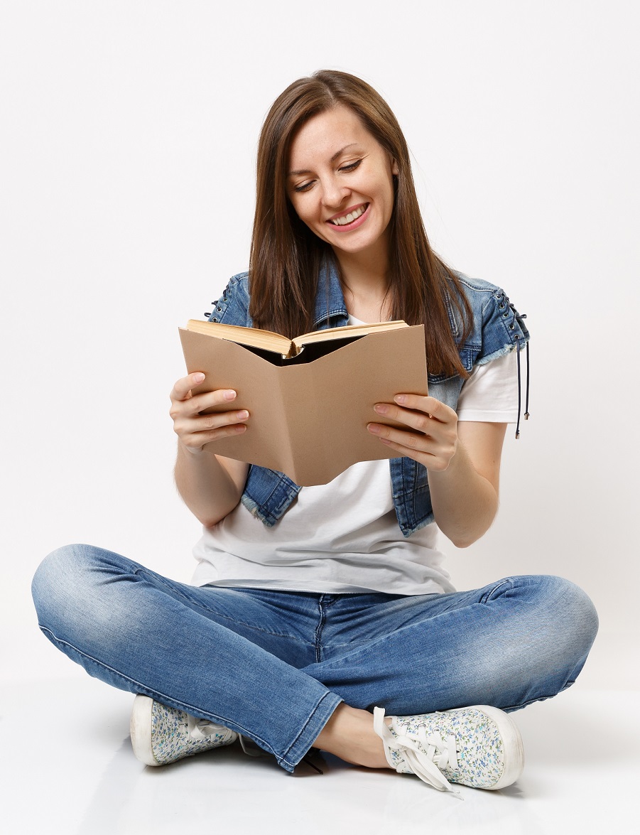 Young casual smiling woman student in denim clothes holding book reading sitting near globe, backpack, school books isolated on white background. Education in high school university college concept